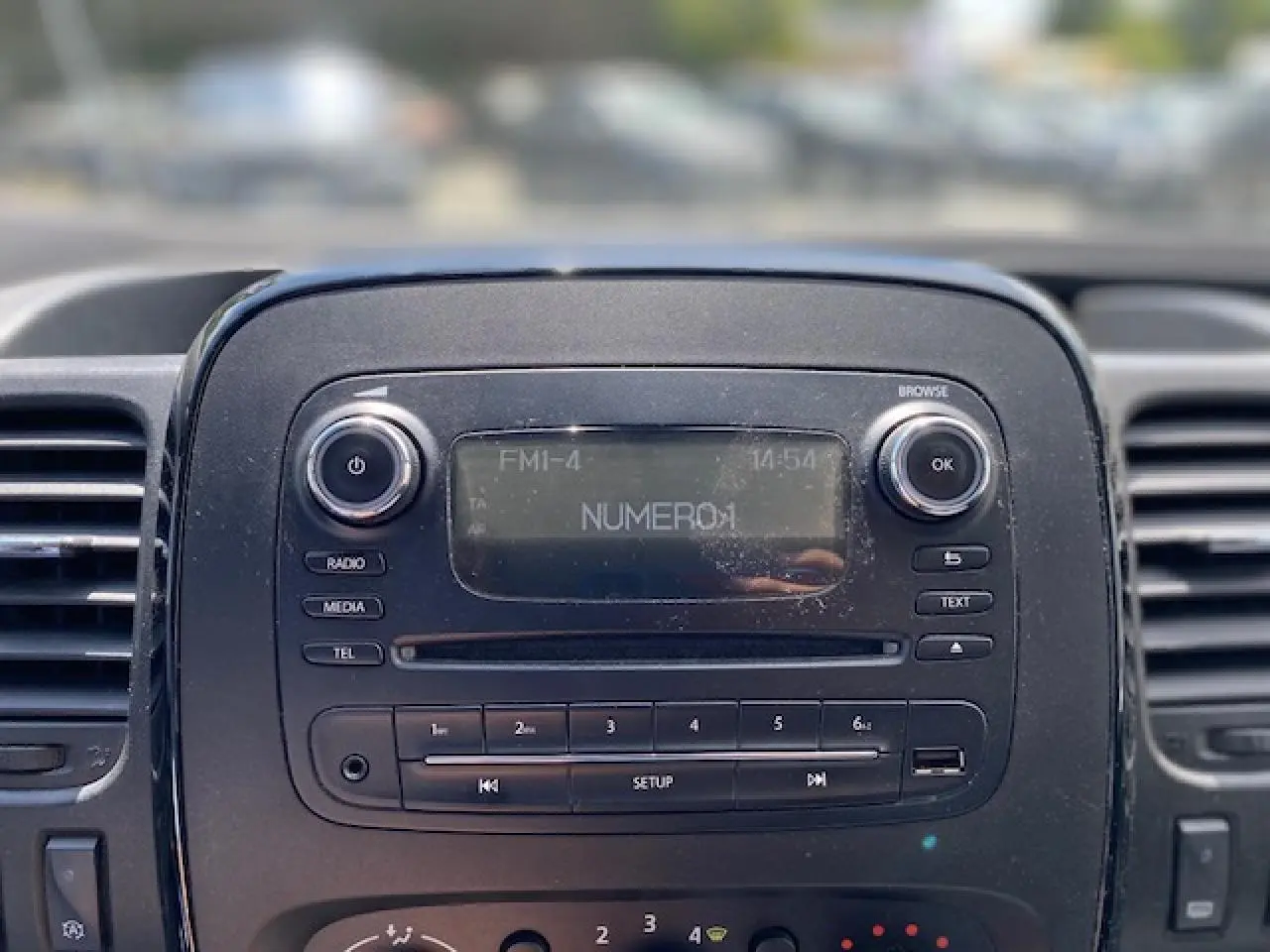 Gros plan sur la console centrale noire de l'Opel Vivaro blanc, affichant la radio FM et les commandes multimédia.