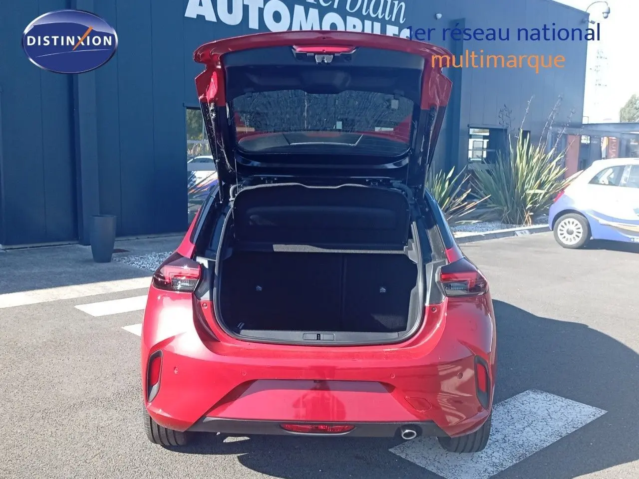 Vue arrière d'une Opel Corsa rouge Kardio métal avec toit noir, coffre ouvert en extérieur sur parking.