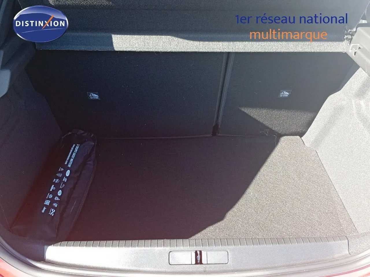 Coffre ouvert de l’Opel Corsa rouge Kardio métal avec toit noir, montrant un espace de chargement vide et un kit de sécurité.