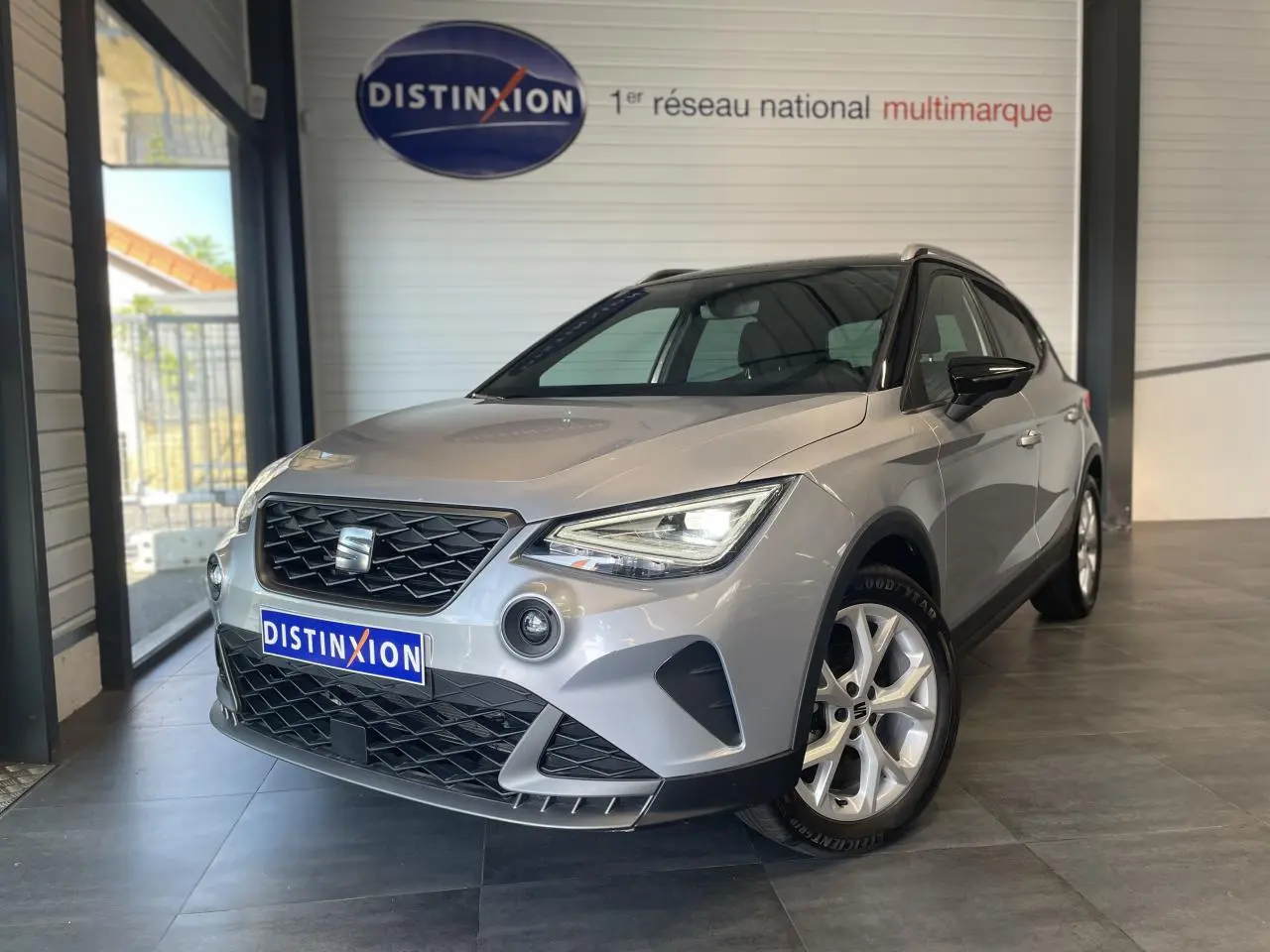 Vue 3/4 avant d'un SEAT Arona 2024 gris clair avec jantes alliage 16 pouces et calandre noire en showroom.