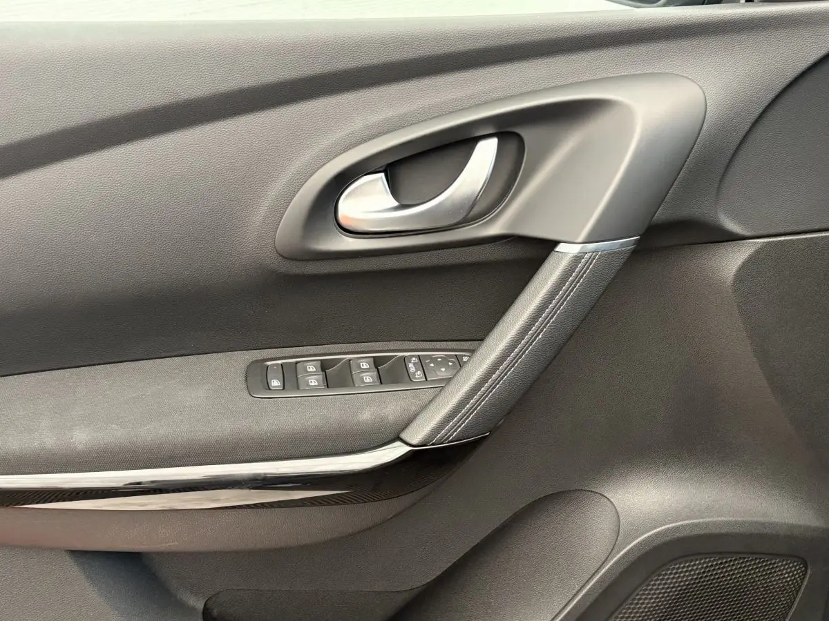 Gros plan sur la porte intérieure côté gauche du Renault Kadjar gris foncé, avec poignée argentée et commandes vitres.