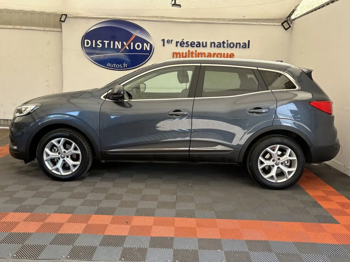 Profil droit d’un Renault Kadjar gris foncé 2019 garé en intérieur avec jantes alliage et barres de toit chromées.