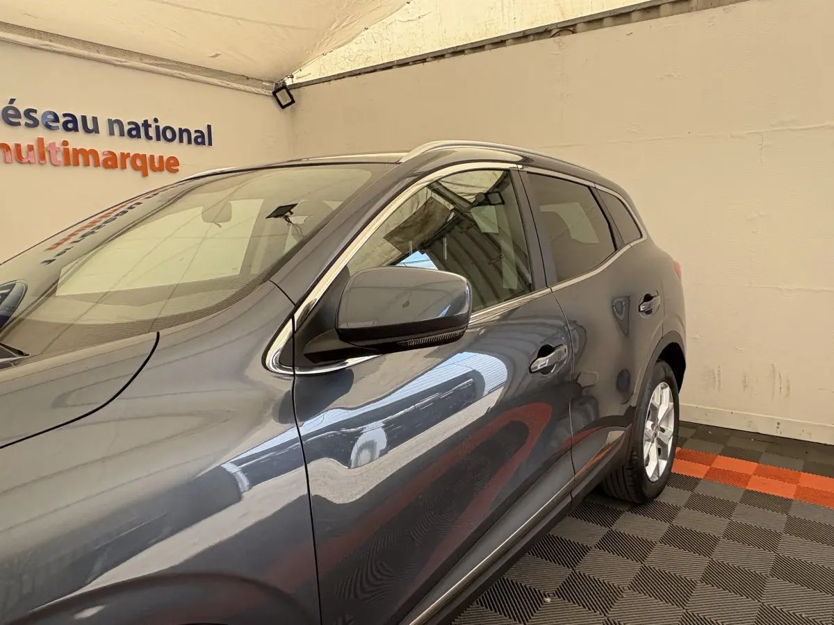 Vue 3/4 avant droit du Renault Kadjar Intens gris foncé, avec rétroviseur et poignées de porte visibles.