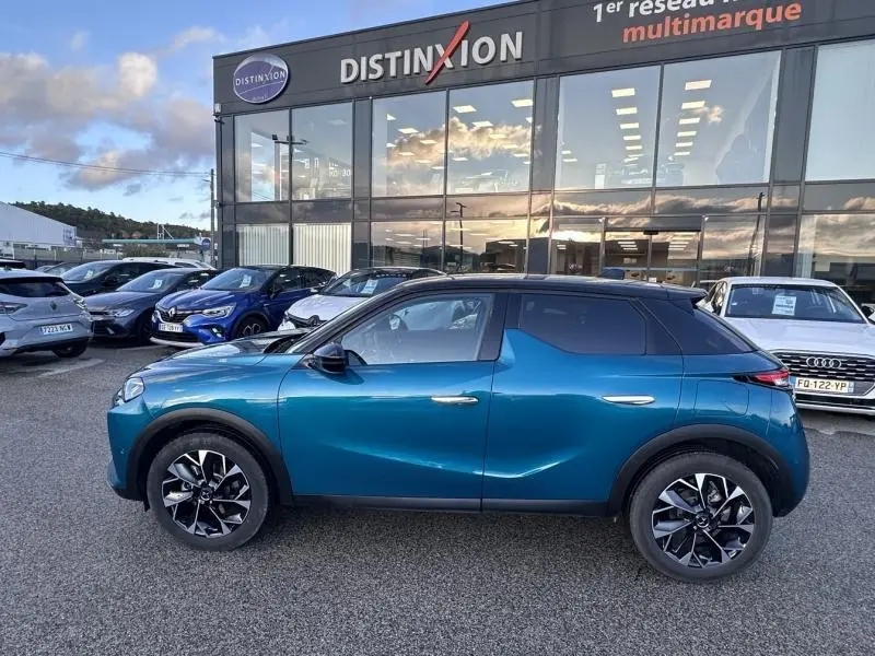 Vue de profil côté gauche d'une DS3 1.2 Hybride bleu métallisé avec jantes alu noires devant un concessionnaire Distinxion.