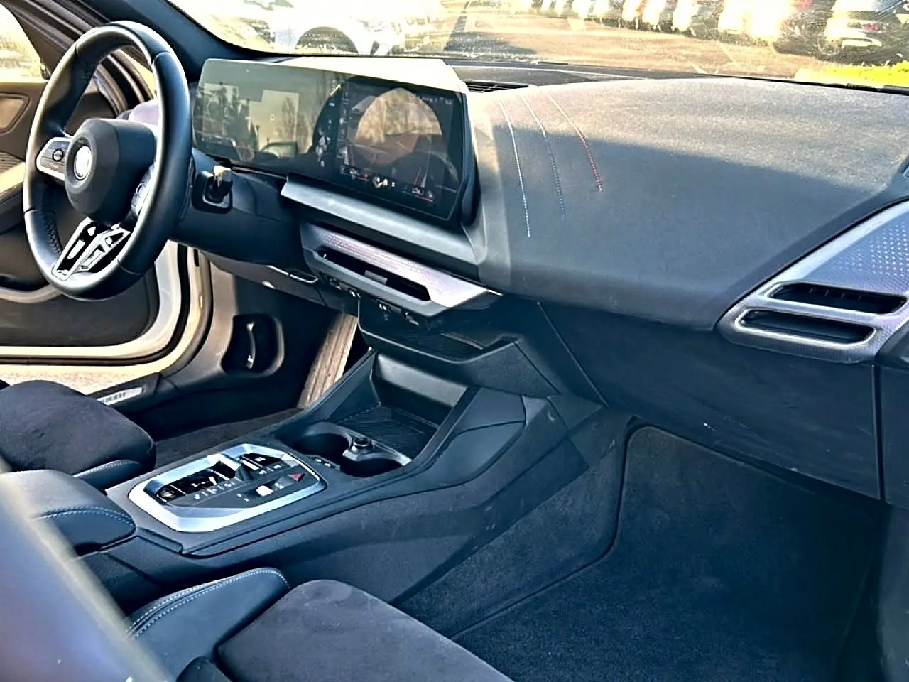 Intérieur BMW Série 1 2025 vu côté passager, tableau de bord et console centrale en tissu noir avec coutures bleues.