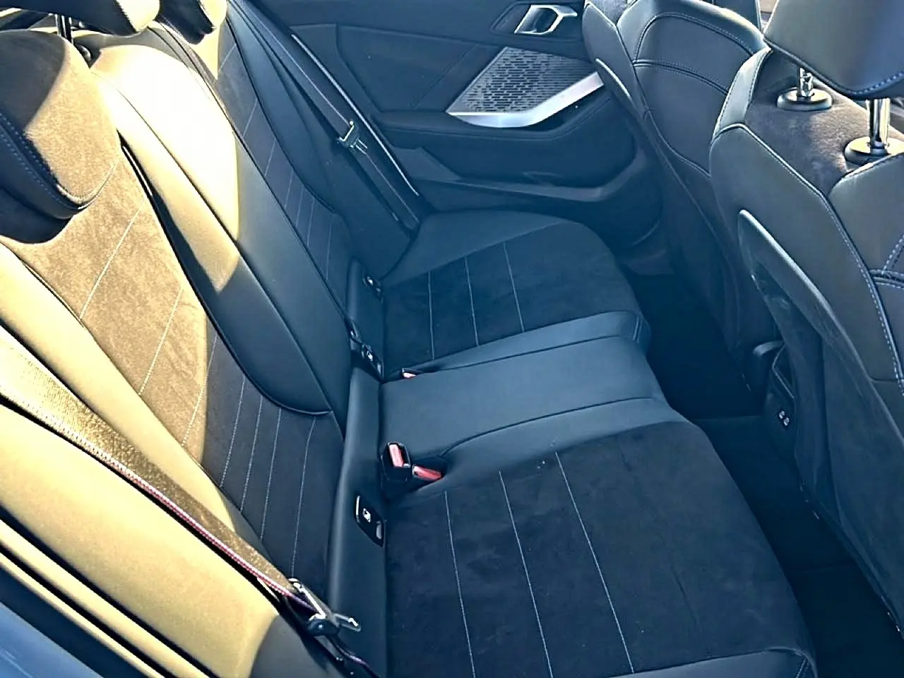 Vue intérieure des sièges arrière en tissu alcantara noir avec surpiqûres bleues d'une BMW Série 1 2025.