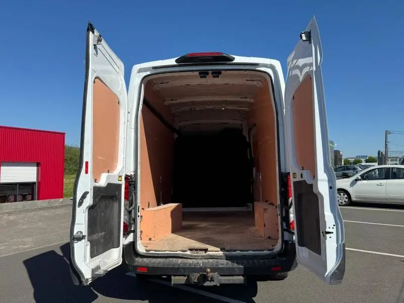 Vue arrière du fourgon Ford Transit blanc glacier 2020 avec portes battantes ouvertes montrant l'espace de chargement vide.
