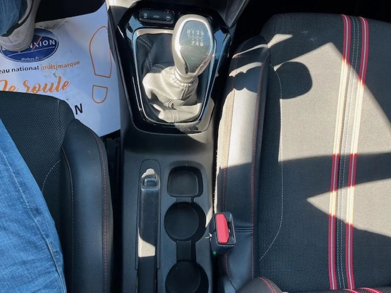 Vue plongeante sur la console centrale d'une Opel Corsa 2021 gris/noir, avec levier de vitesse manuel et sièges sport rayés rouges.