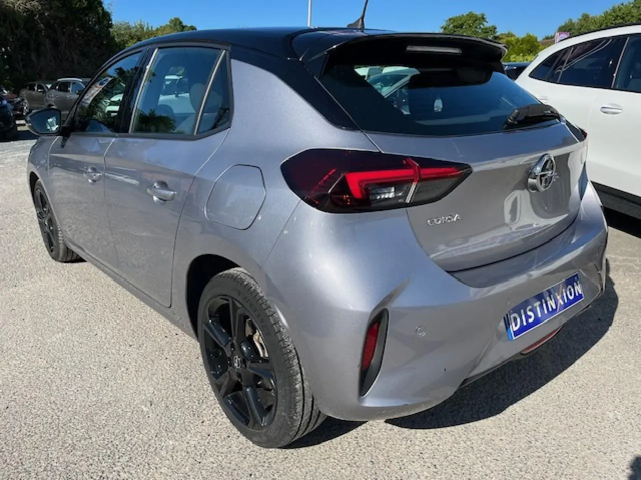 Vue 3/4 arrière droite d'une Opel Corsa gris métallisé avec toit noir et jantes noires sur un parking extérieur.