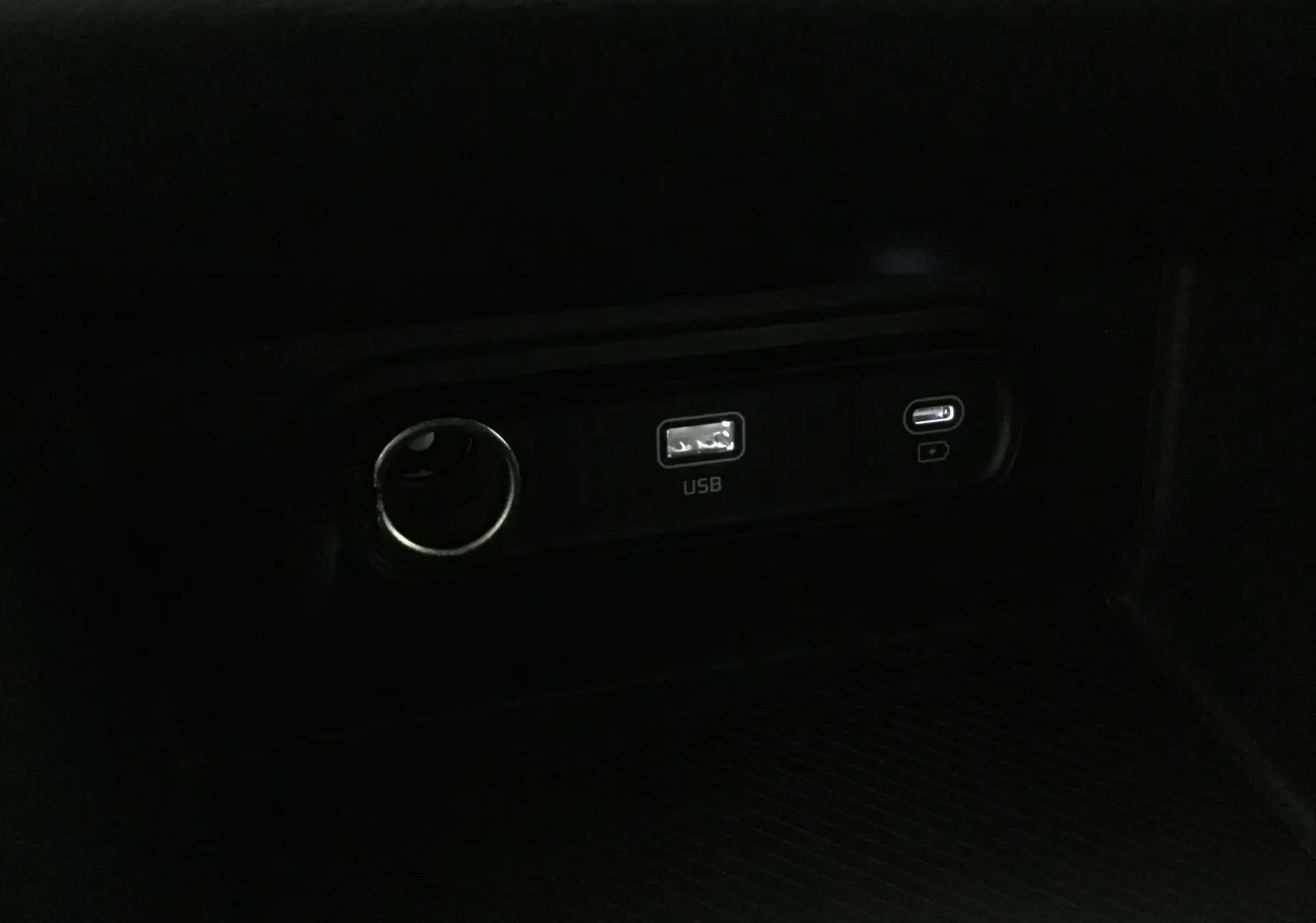 Prise USB et port allume-cigare en gros plan dans l'habitacle du Kia Sportage gris Sirius 2025.