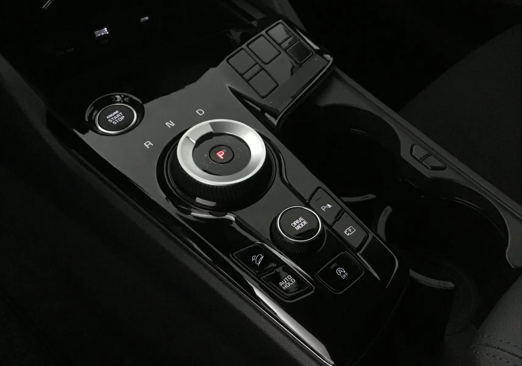 Gros plan sur la console centrale noire brillante du Kia Sportage 2025 avec sélecteur rotatif de boîte auto et bouton start/stop.