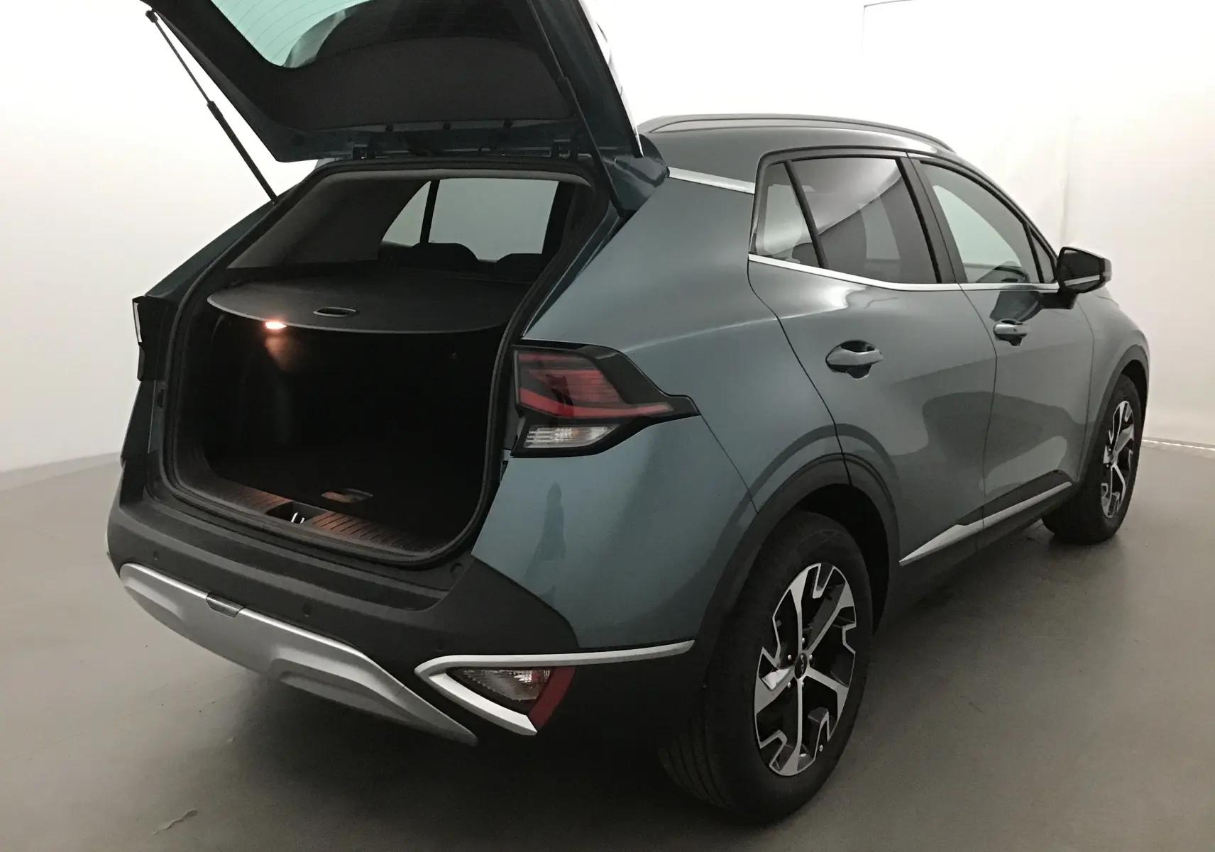 KIA SPORTAGE gris Sirius vu de l'arrière côté droit avec coffre ouvert et feux arrière LED allumés.