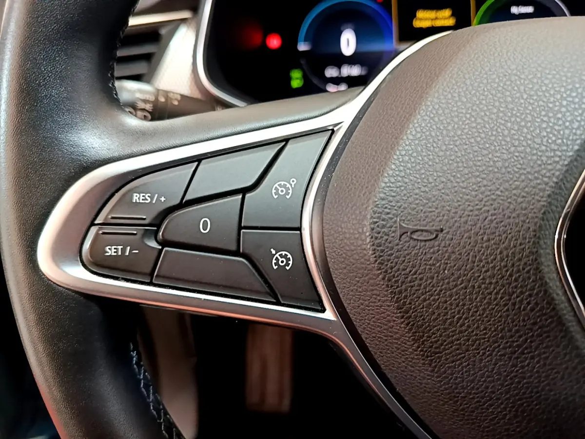 Gros plan sur les commandes de régulateur de vitesse au volant noir du Renault Arkana bleu, tableau de bord numérique en arrière-plan.