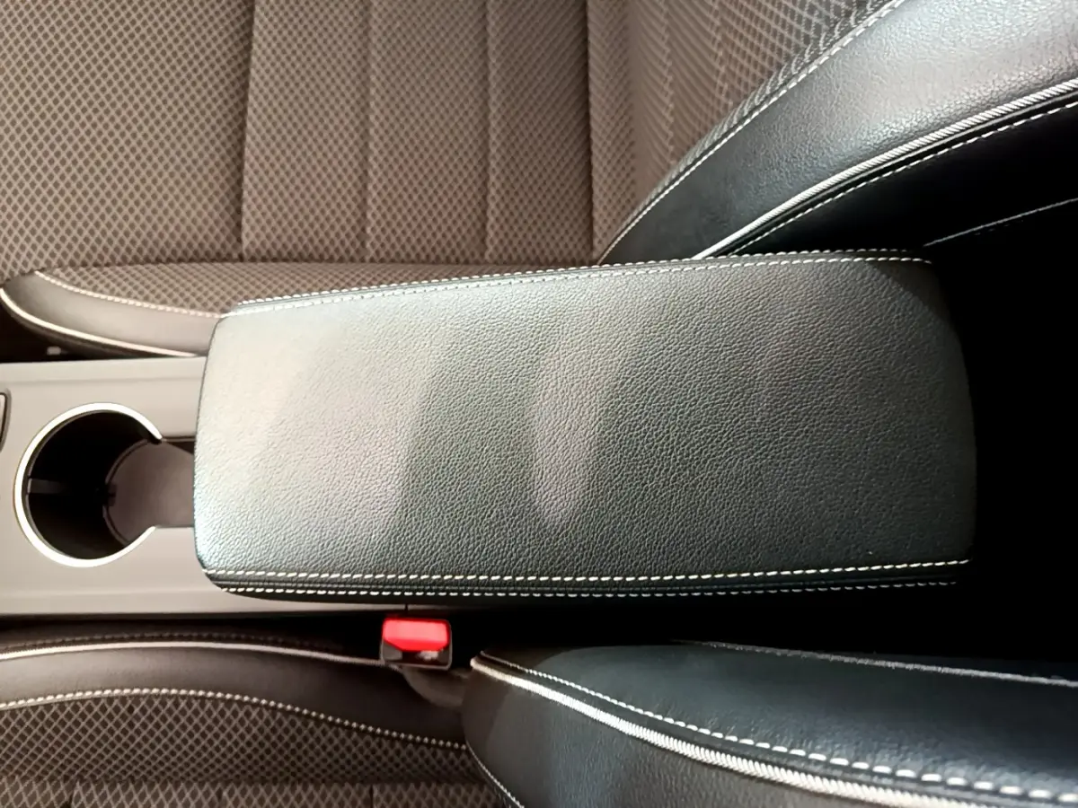 Gros plan sur l'accoudoir central en cuir noir avec surpiqûres blanches, entouré des sièges avant en tissu marron.