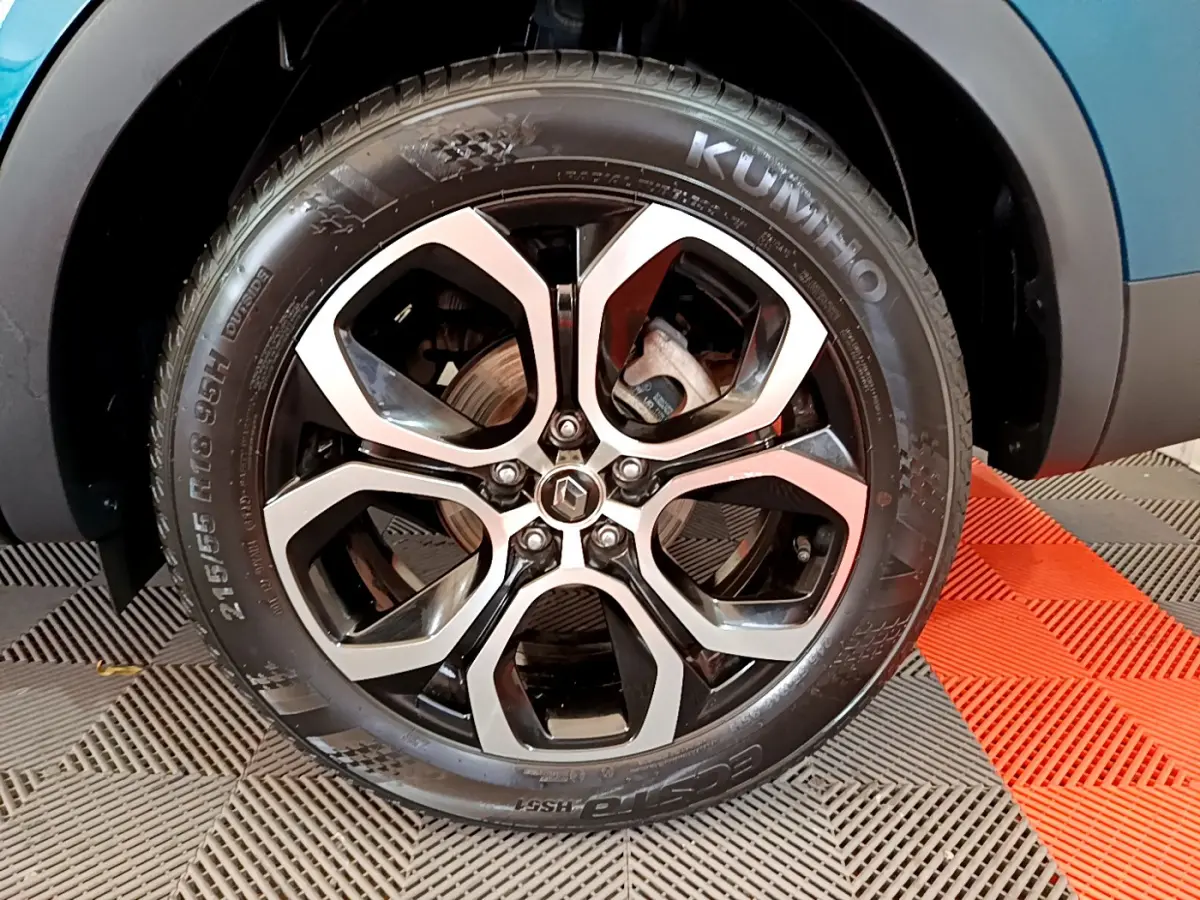 Gros plan sur la roue avant droite du Renault Arkana bleu, jante alliage noire et argent avec logo Renault central.