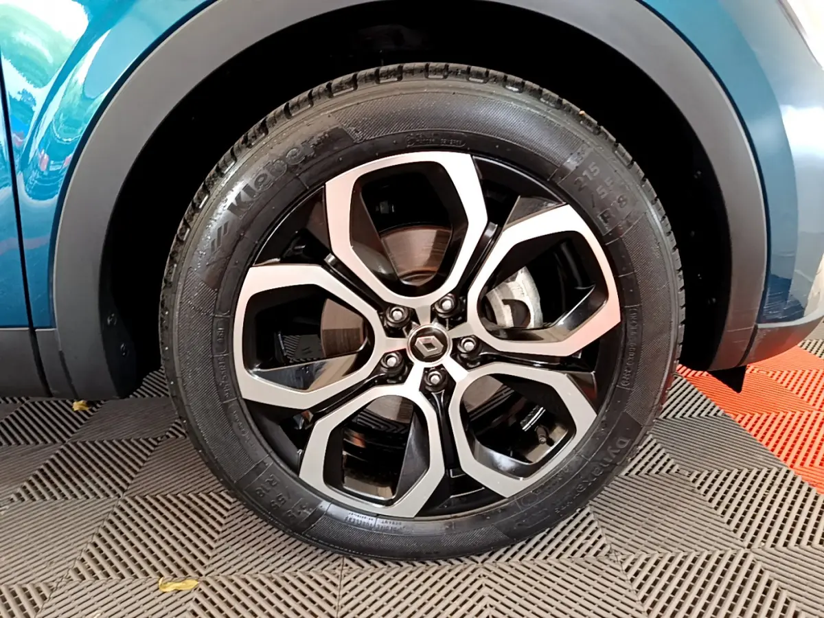 Gros plan sur la roue avant gauche bleu métallisé d'une Renault Arkana Techno E-Tech hybride avec jante alliage noire et argent.