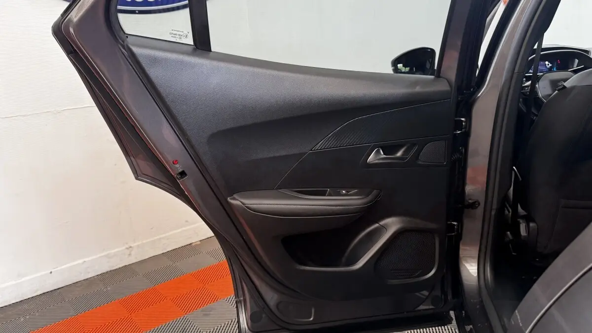 Vue intérieure côté gauche de la porte arrière ouverte d’un Peugeot 2008 gris foncé, avec garniture noire et commande de vitre.