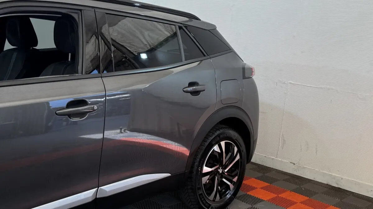 Vue latérale arrière droite d’un Peugeot 2008 gris foncé avec jantes noires et détails chromés sur les portes.