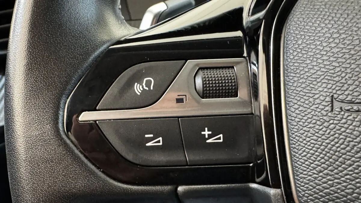 Gros plan sur les commandes vocales et volume du volant cuir noir du Peugeot 2008 gris foncé, version Allure Pack 2022.
