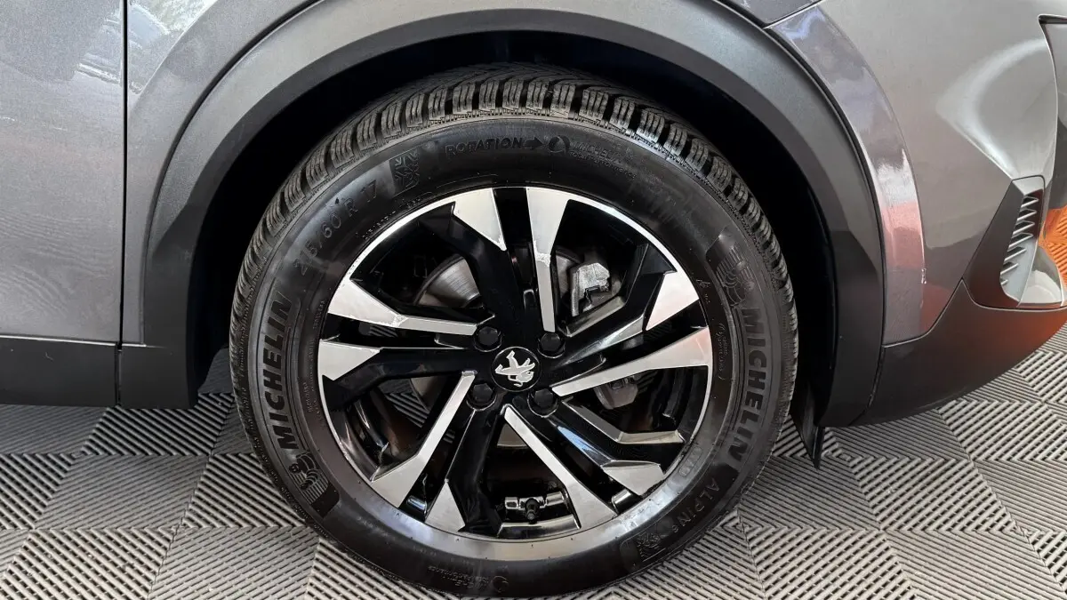 Gros plan sur la roue avant droite d’un Peugeot 2008 gris foncé, avec jante alliage noire et argentée au design moderne.