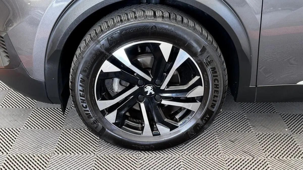 Gros plan sur la roue avant droite du Peugeot 2008 gris foncé, jante alliage noire et argent avec logo lion central.
