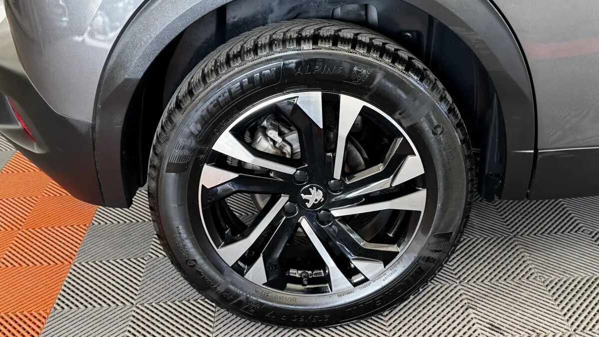 Gros plan sur la roue arrière droite gris foncé d’un Peugeot 2008 avec jante alliage noir et argent et pneu Michelin Alpine.