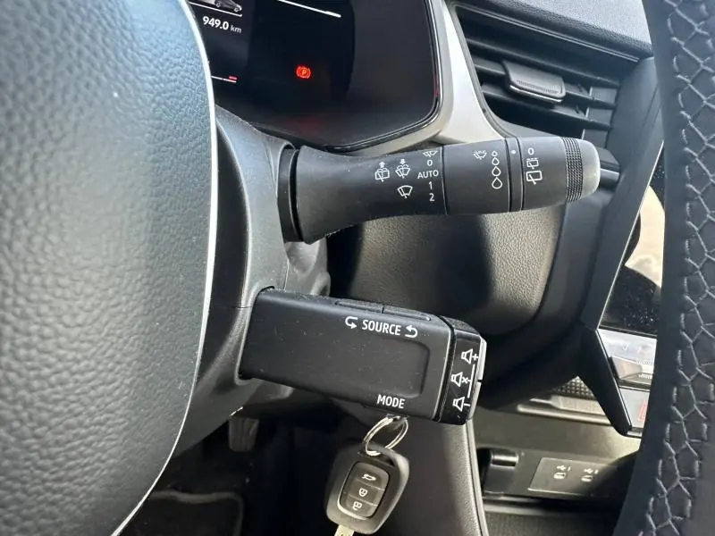 Gros plan sur les commandes au volant noir du Renault Captur 2025, avec clé insérée et tableau de bord partiellement visible.