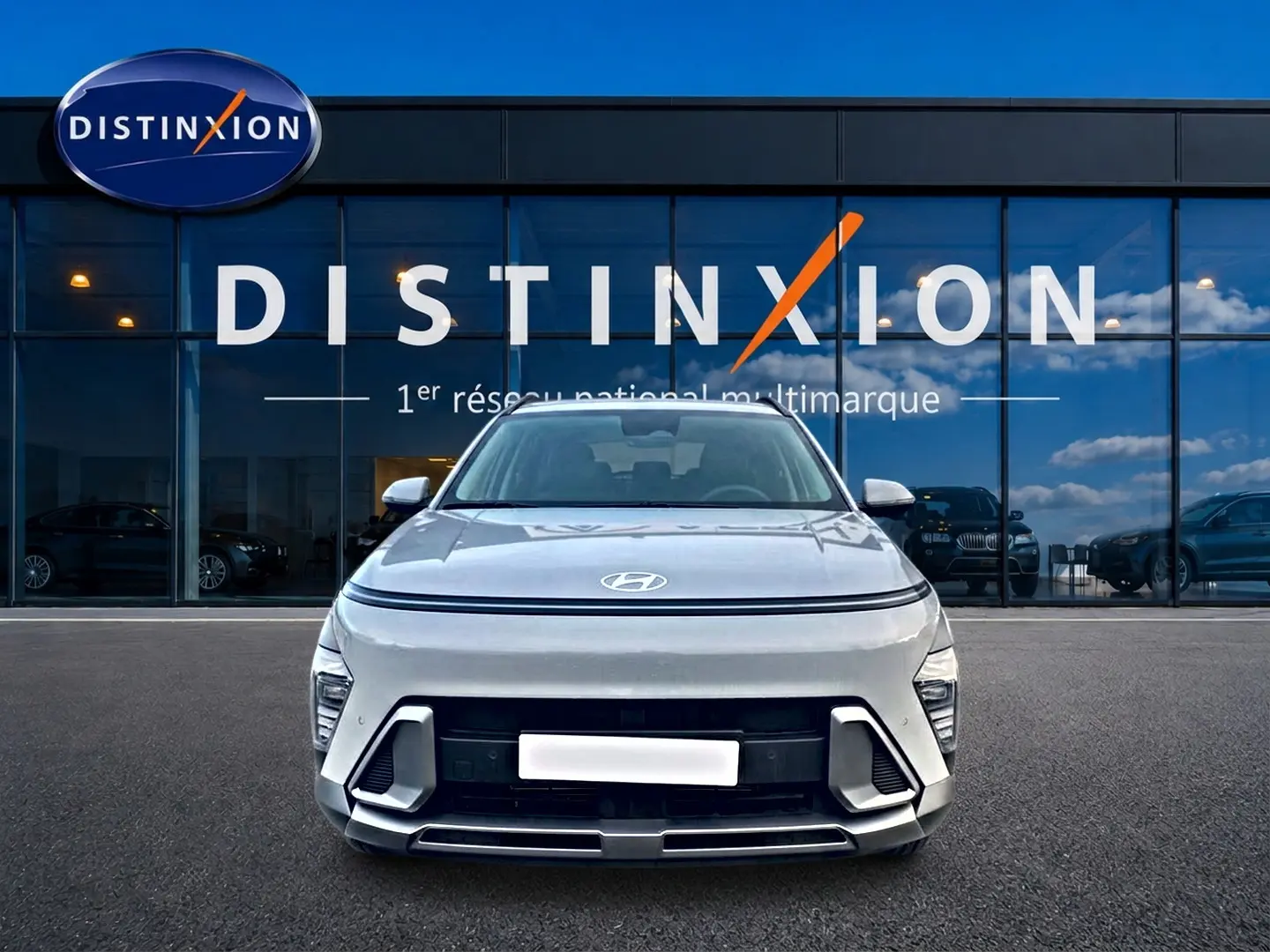 Vue avant d'un Hyundai Kona gris 2025 avec calandre et feux LED, devant une vitrine Distinxion.