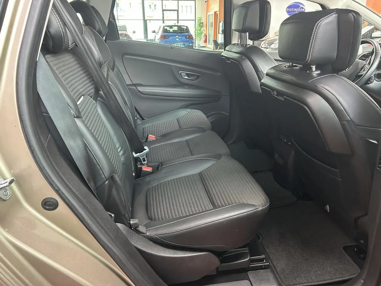 Vue côté gauche arrière du Renault Scénic Grand IV marron clair, mettant en valeur les sièges arrière en similicuir noir avec surpiqûres blanches.