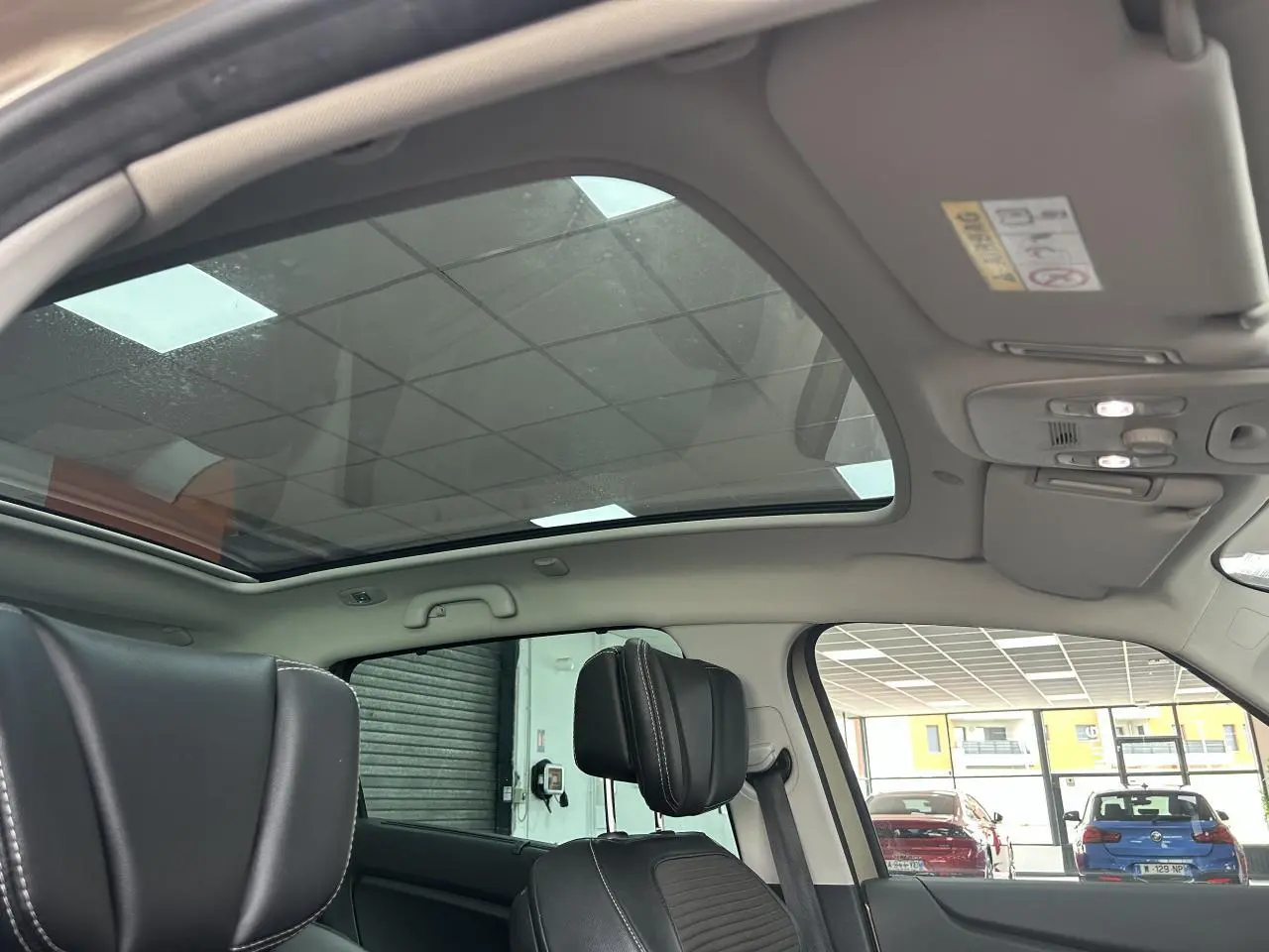 Vue intérieure du toit panoramique en verre du Renault Scenic Grand IV marron clair, avec sièges avant en similicuir noir.