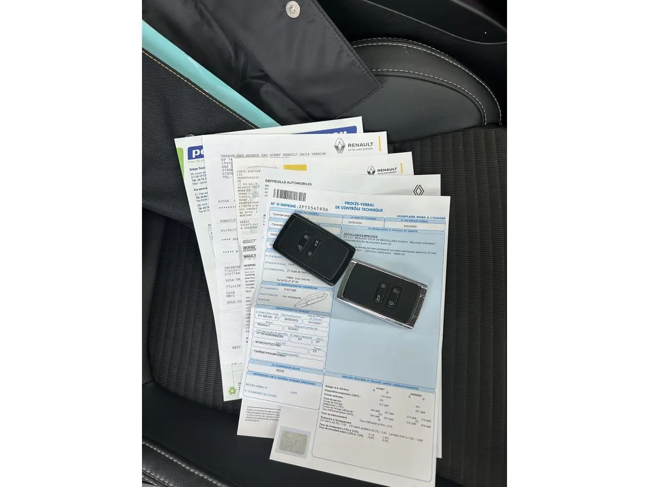 Vue plongeante sur siège avant noir avec documents Renault et deux clés de voiture posées dessus.