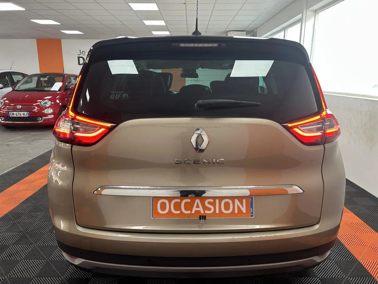 Vue arrière d'un Renault Scénic Grand IV marron clair avec feux LED allumés dans un showroom.