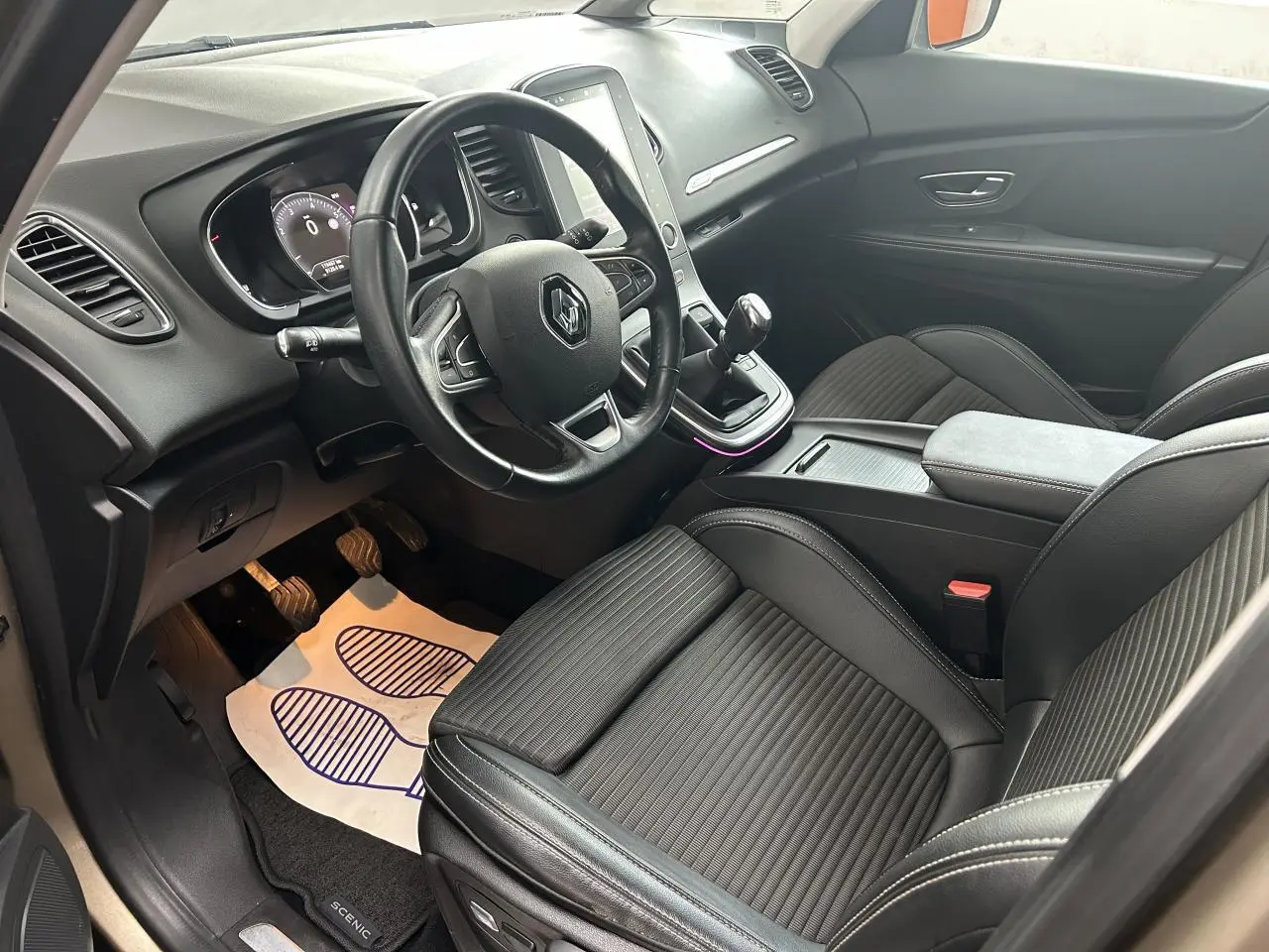 Vue intérieure côté conducteur du Renault Scenic Grand IV avec sièges noirs en similicuir et console centrale moderne.