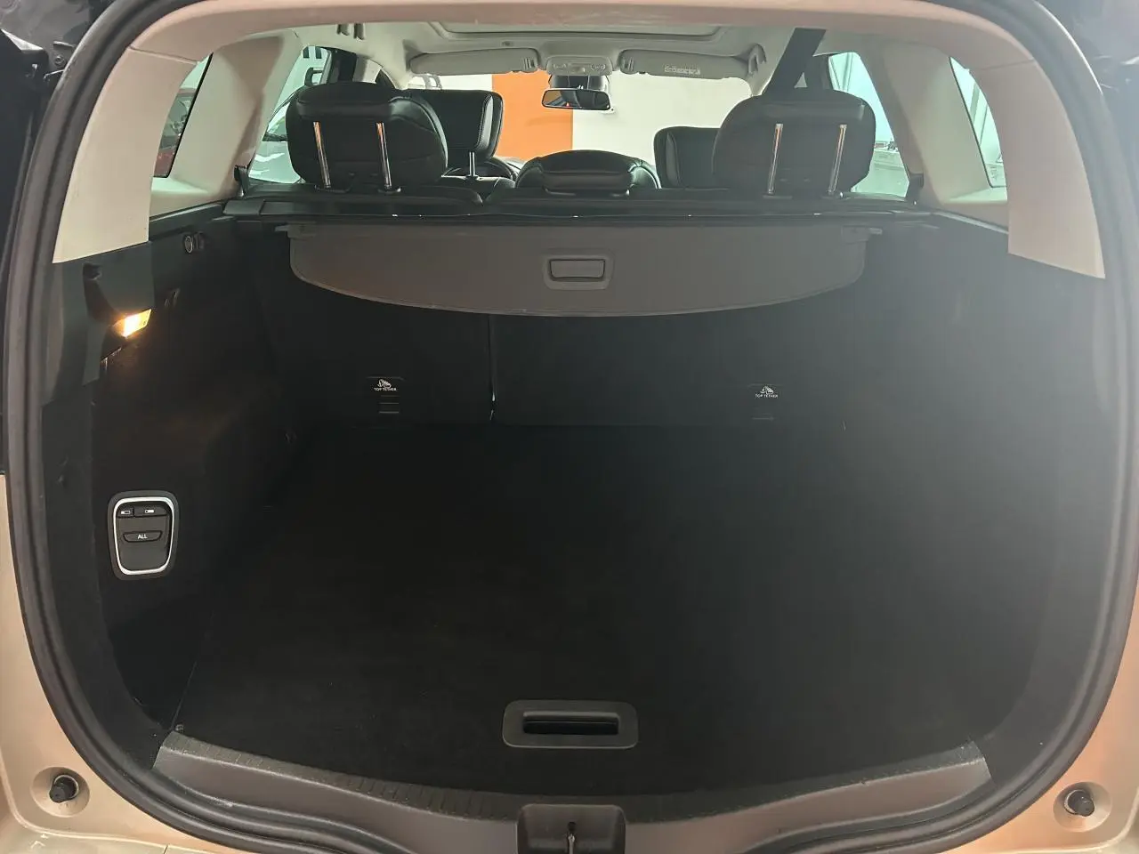 Coffre ouvert vu de l'arrière d'un Renault Scenic Grand IV marron clair avec cache-bagages et sièges arrière visibles.