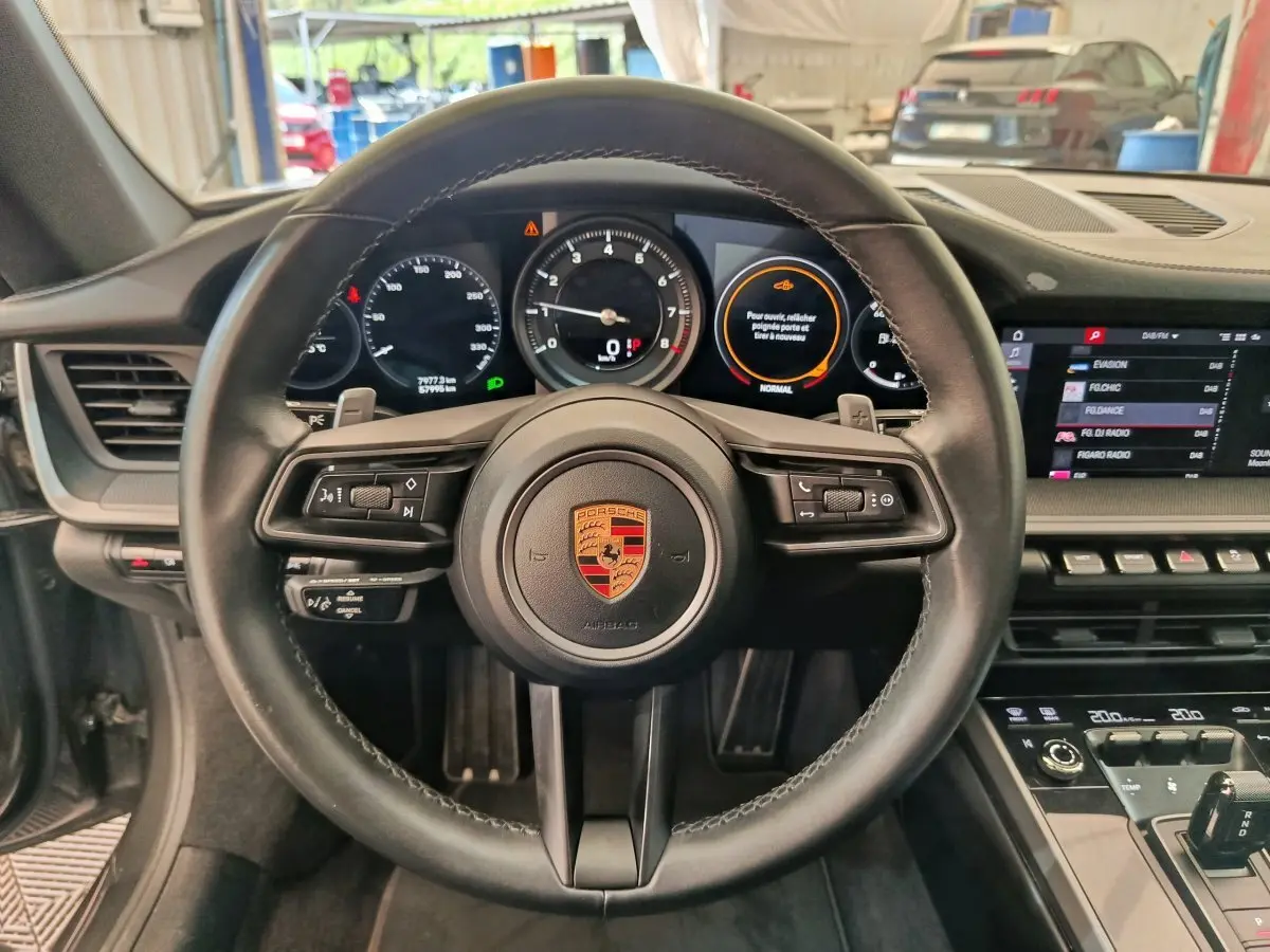 Vue intérieure centrée sur le volant cuir noir de la Porsche 911 Carrera 4S avec tableau de bord numérique et écran tactile.