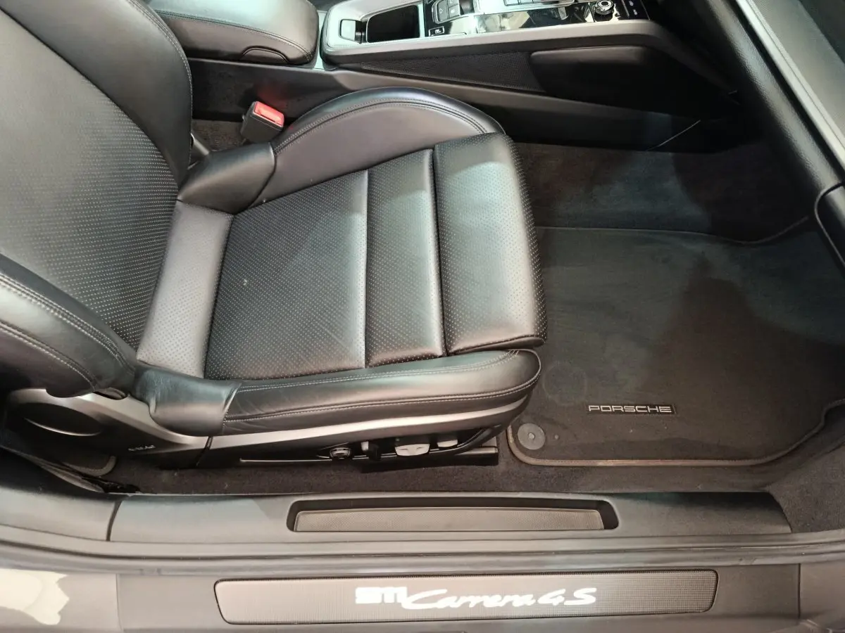 Vue intérieure côté conducteur sur le siège en cuir noir et tapis de sol Porsche d'une 911 Carrera 4S Coupé gris foncé.
