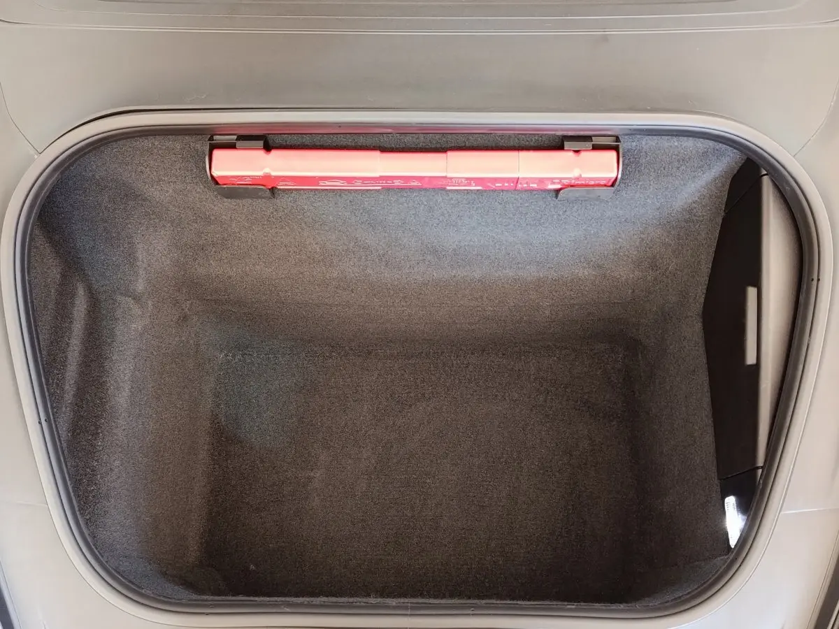 Coffre avant ouvert vu de dessus, intérieur gris foncé avec trousse de secours rouge visible sur le bord.