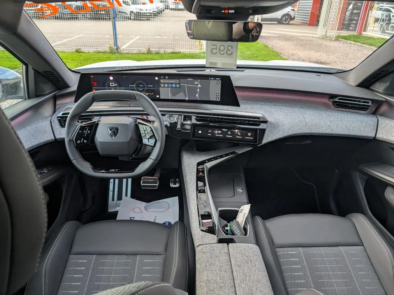 Vue intérieure avant du Peugeot 3008 GT 2025, tableau de bord et volant compact avec finitions tissu gris et noir laqué.