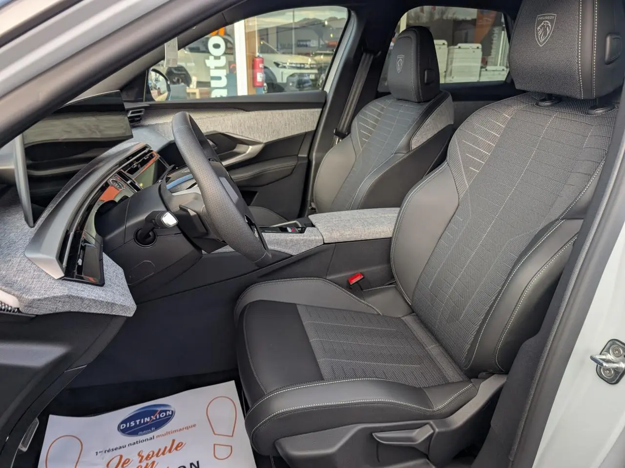 Vue intérieure côté conducteur du Peugeot 3008 blanc 2025, sièges tissu et cuir gris avec logo Peugeot brodé.
