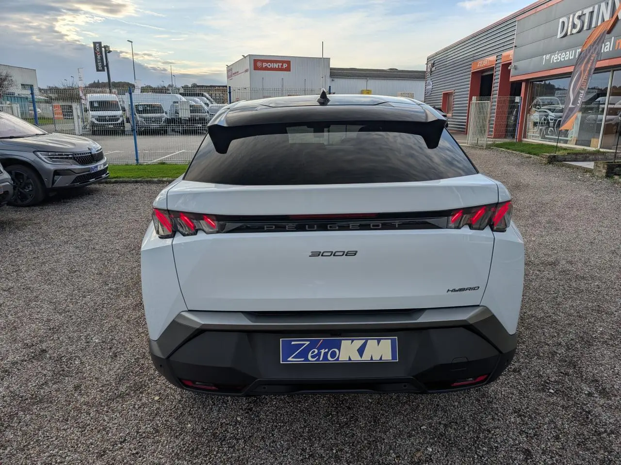 Vue arrière d'un Peugeot 3008 blanc hybride 2025 avec feux arrière à griffes LED et bandeau noir laqué entre les feux.