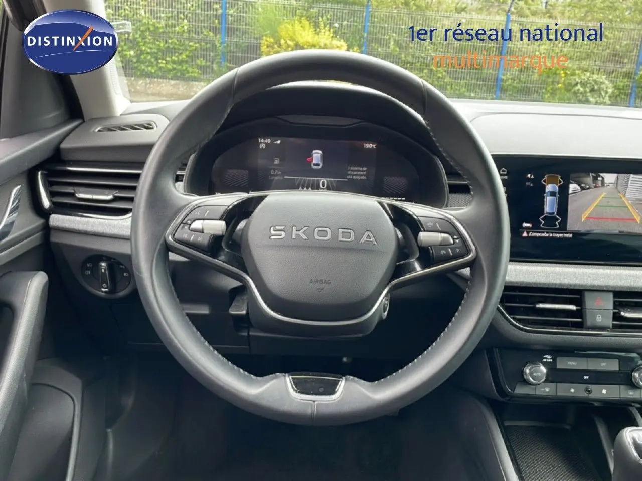 Vue intérieure centrée sur le volant SKODA d'une Scala 2025, avec tableau de bord numérique et écran de caméra de recul.