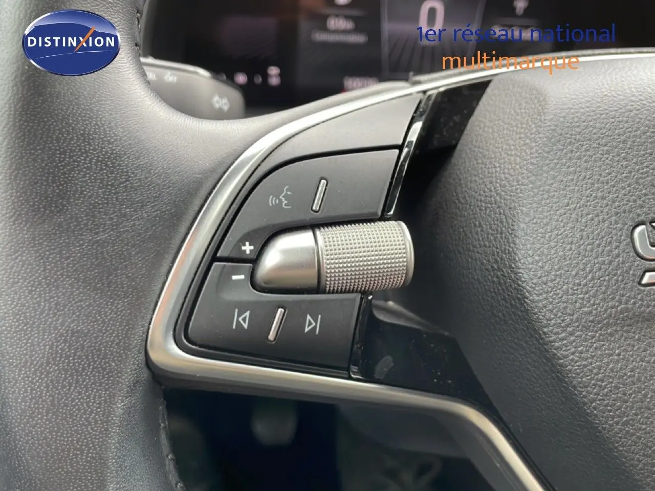 Gros plan sur les commandes gauche du volant en cuir noir d’une Skoda Scala 2025, avec molette métallique texturée.