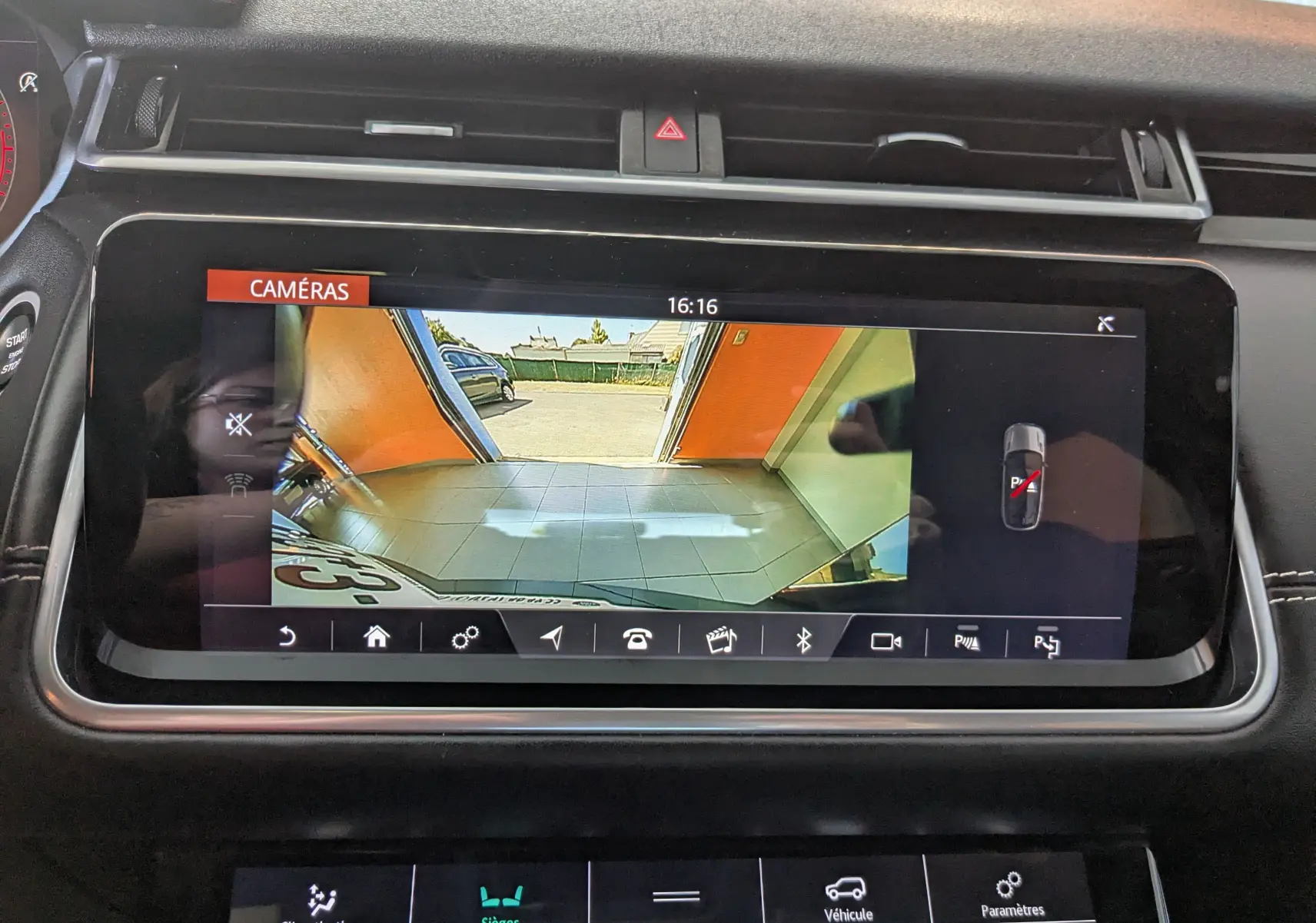 Écran central du Range Rover Velar noir montrant la caméra de recul avec vue sur un garage et l'extérieur.