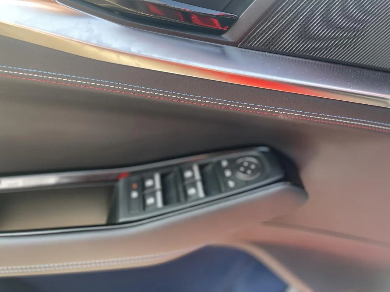 Détail de la porte côté gauche de la Renault Rafale 2025 rouge avec surpiqûres tricolores et commandes de vitres.