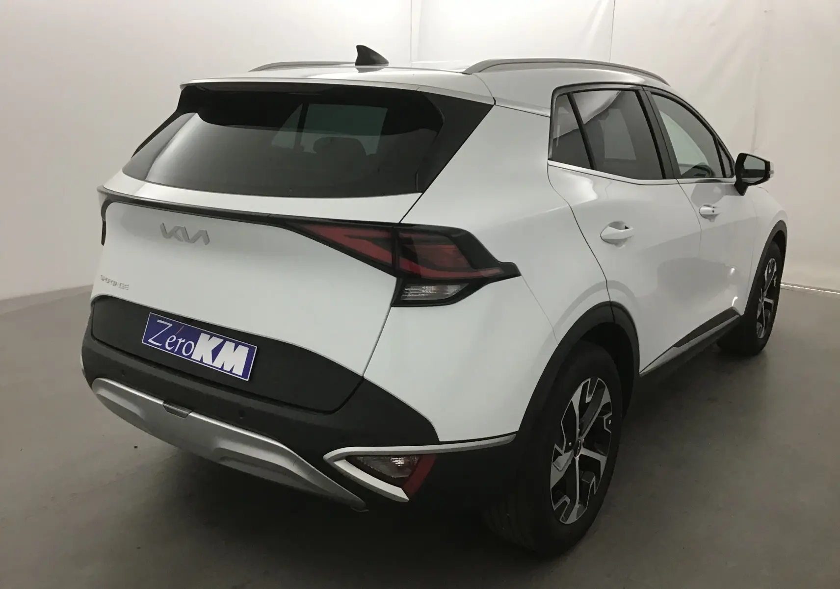 Vue 3/4 arrière droite d'un Kia Sportage blanc 2025 avec feux arrière LED et jantes alliage noires.