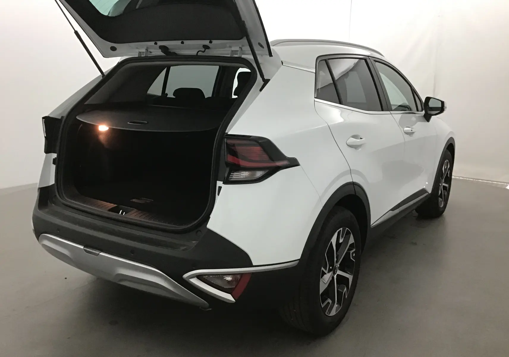 Vue 3/4 arrière droite du Kia Sportage blanc 2025 avec coffre ouvert et feux arrière LED distinctifs.