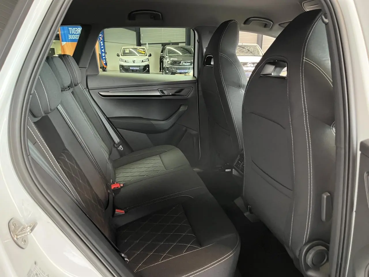 Vue intérieure côté gauche sur la banquette arrière noire avec surpiqûres blanches du Skoda Karoq Sportline blanc 2025.