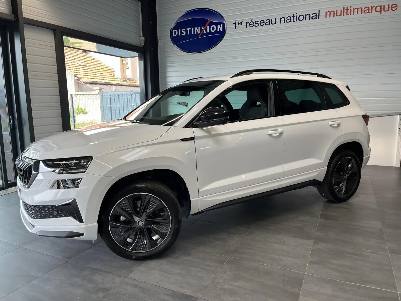 Vue de profil droit du SUV blanc Skoda Karoq 2025 version Sportline avec jantes noires et toit noir en showroom.