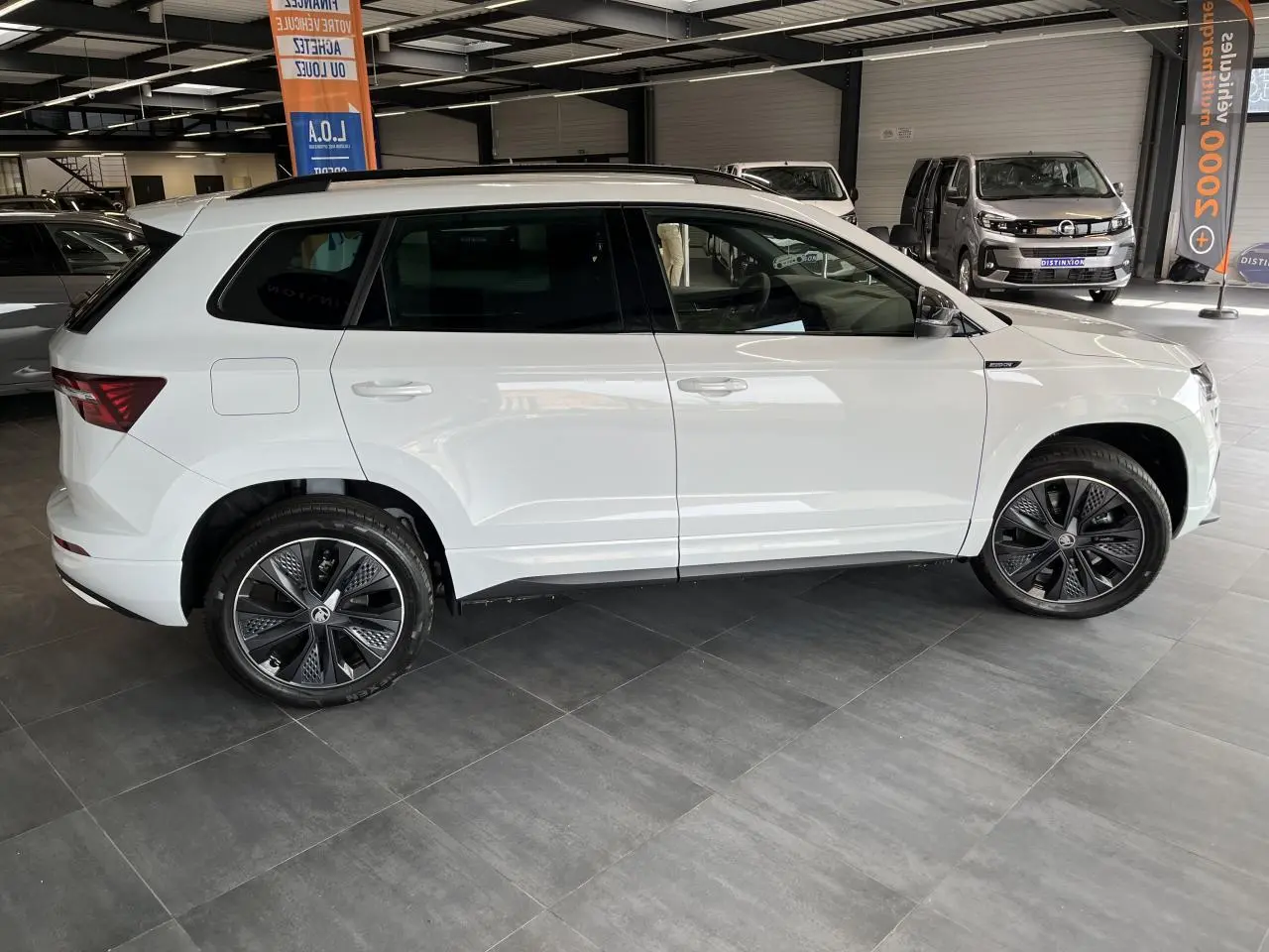 Vue latérale droite d'un SUV Skoda Karoq blanc 2025 avec jantes alliage noires et badges Sportline visibles.
