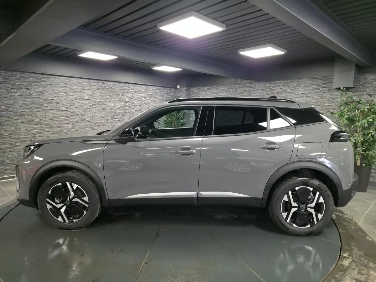 Vue de profil côté gauche d'un Peugeot 2008 gris métallisé avec jantes alliage bi-ton noir et toit noir dans un intérieur showroom.
